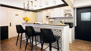 A modern kitchen with a bar area, black bar stools, pendant lights, and patterned backsplash. - Pillows Co-Living (Kowloon)