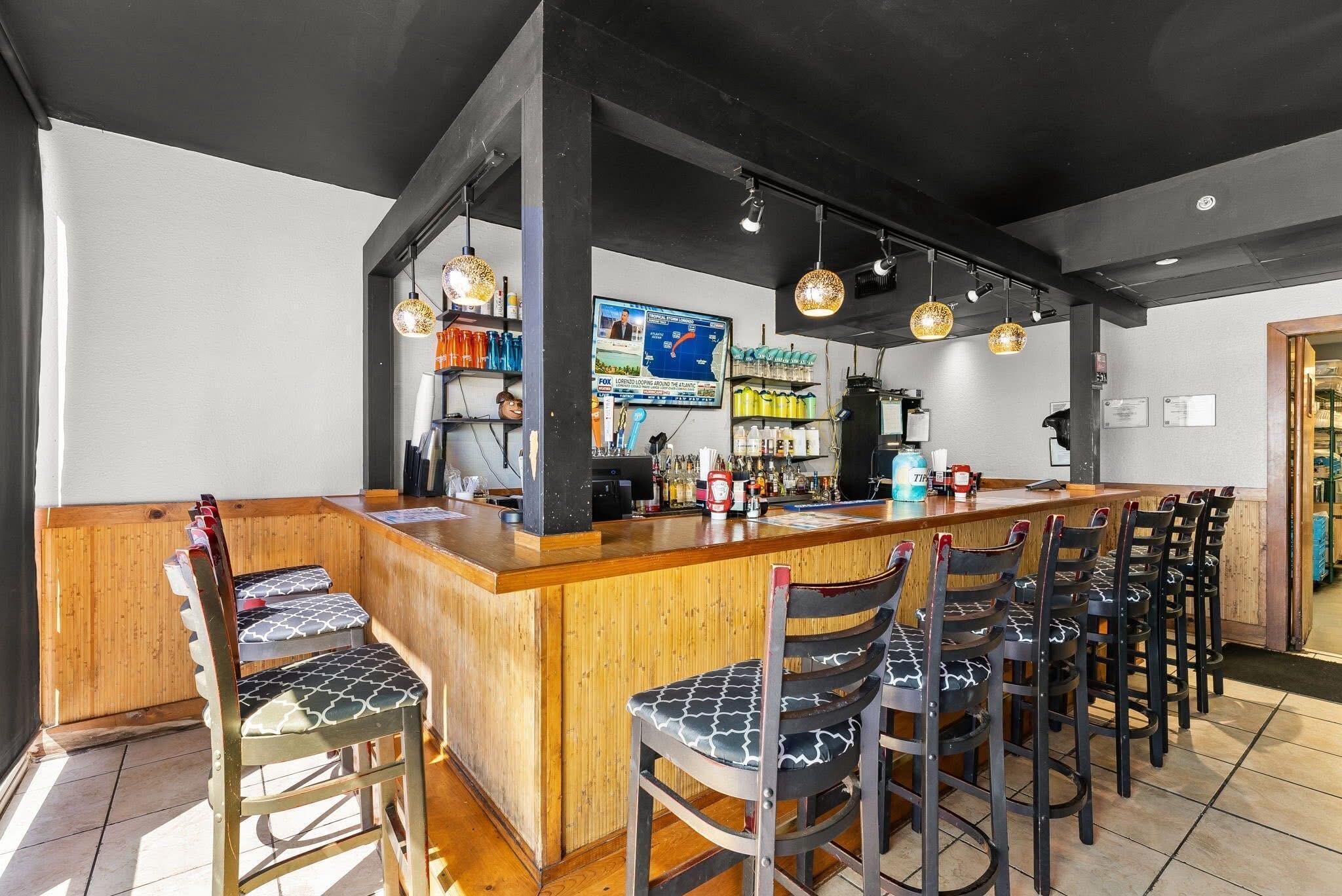 Een bar met een houten toonbank, verschillende barkrukken en hangende吊り下げ式吊り下げライト.