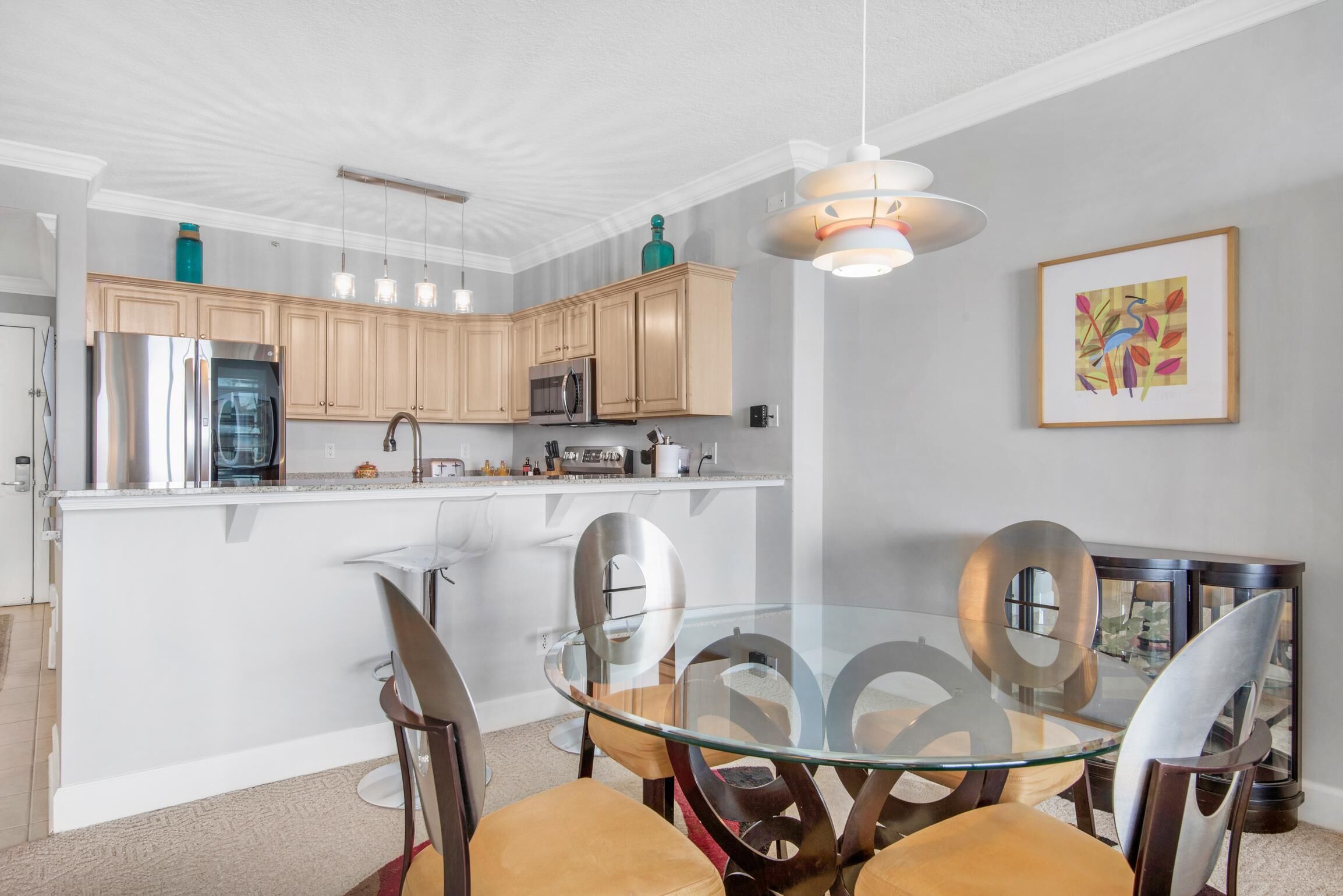 A modern kitchen with wooden cabinets, stainless steel appliances, and a glass dining table with chairs.