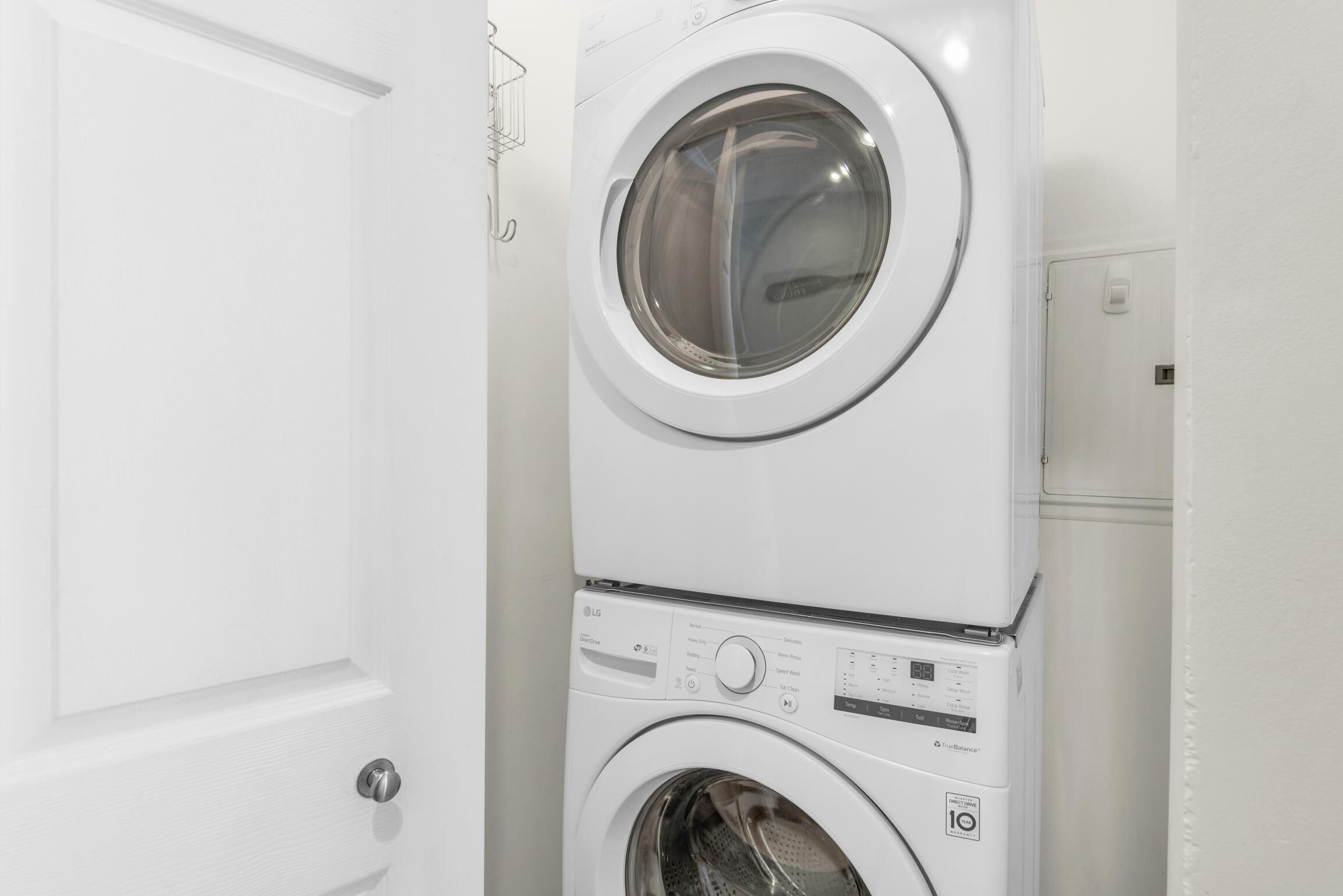 Lavadora y secadora apiladas en una habitación con paredes blancas y una puerta.