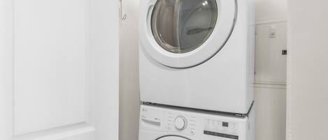 Lavadora y secadora apiladas en una habitación con paredes blancas y una puerta.