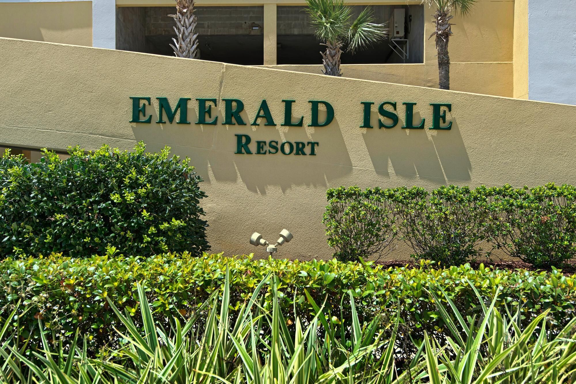 The exterior of Emerald Isle Resort with a signboard, surrounded by well-maintained hedges and palm trees.