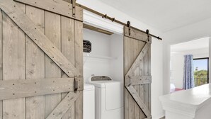 A laundry room with a wooden sliding door, a washing machine, and a sign indicating laundry services. - Sandprints A12 (Miramar Beach)