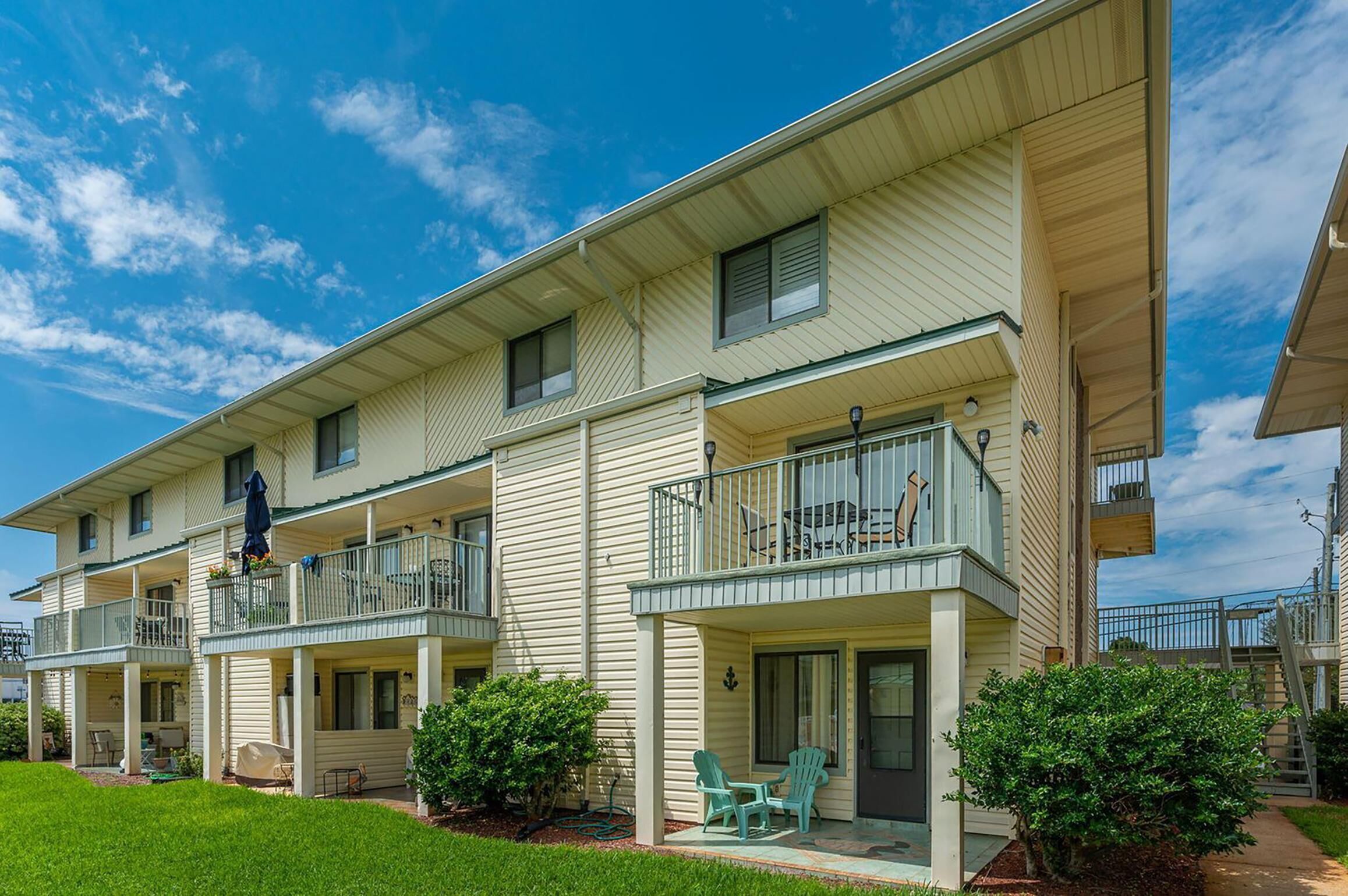 A multi-story residential building with balconies, a covered porch, and a well-maintained lawn.