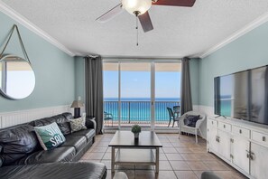 A living room with a view of the ocean, a ceiling fan, a TV, and a sofa with a pillow. - Majestic Beach Towers 1-1302 (Panama City Beach)