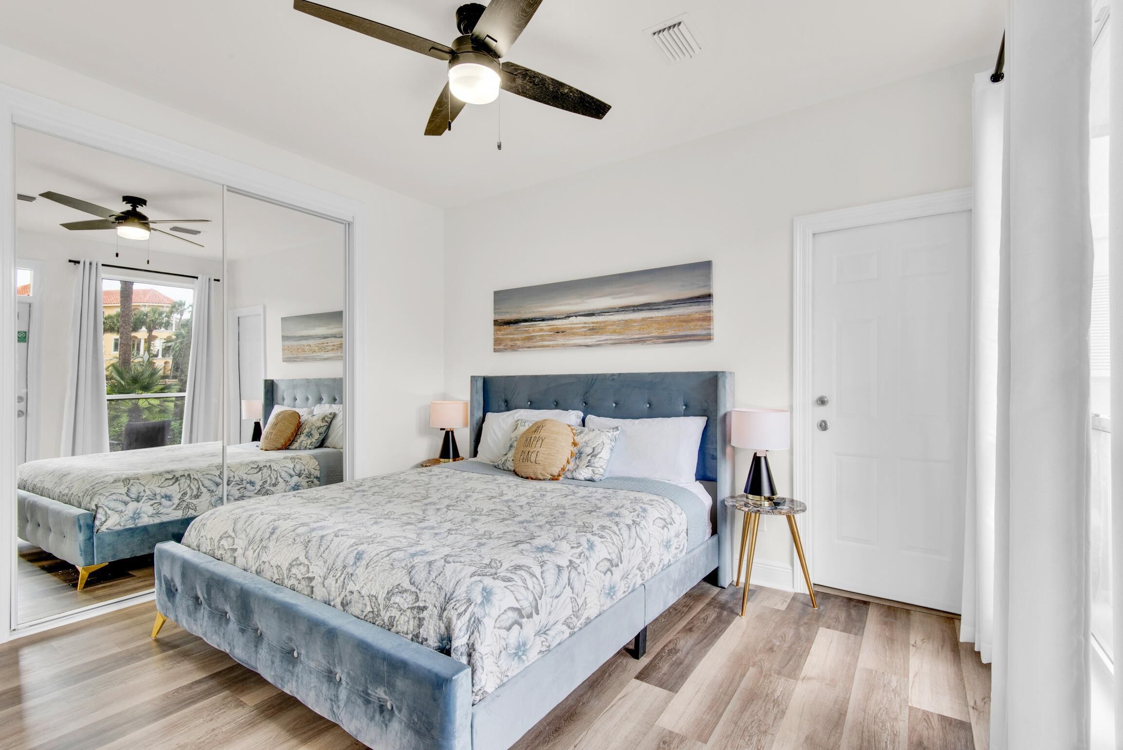 Une chambre avec deux lits, un ventilateur de plafond, un tableau et une porte.