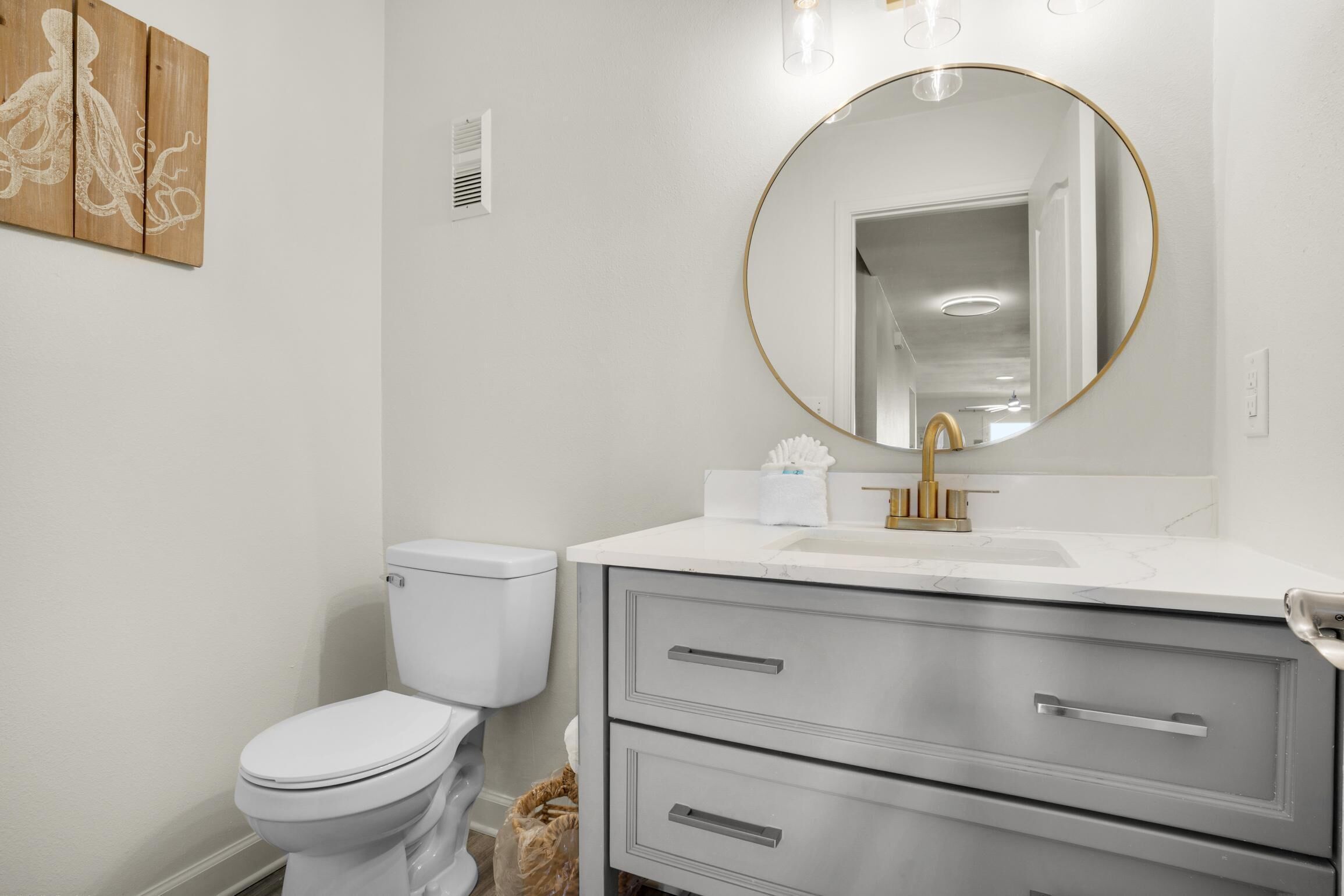 A bathroom with a white toilet, a vanity with a gold faucet, and a round mirror with a gold frame.