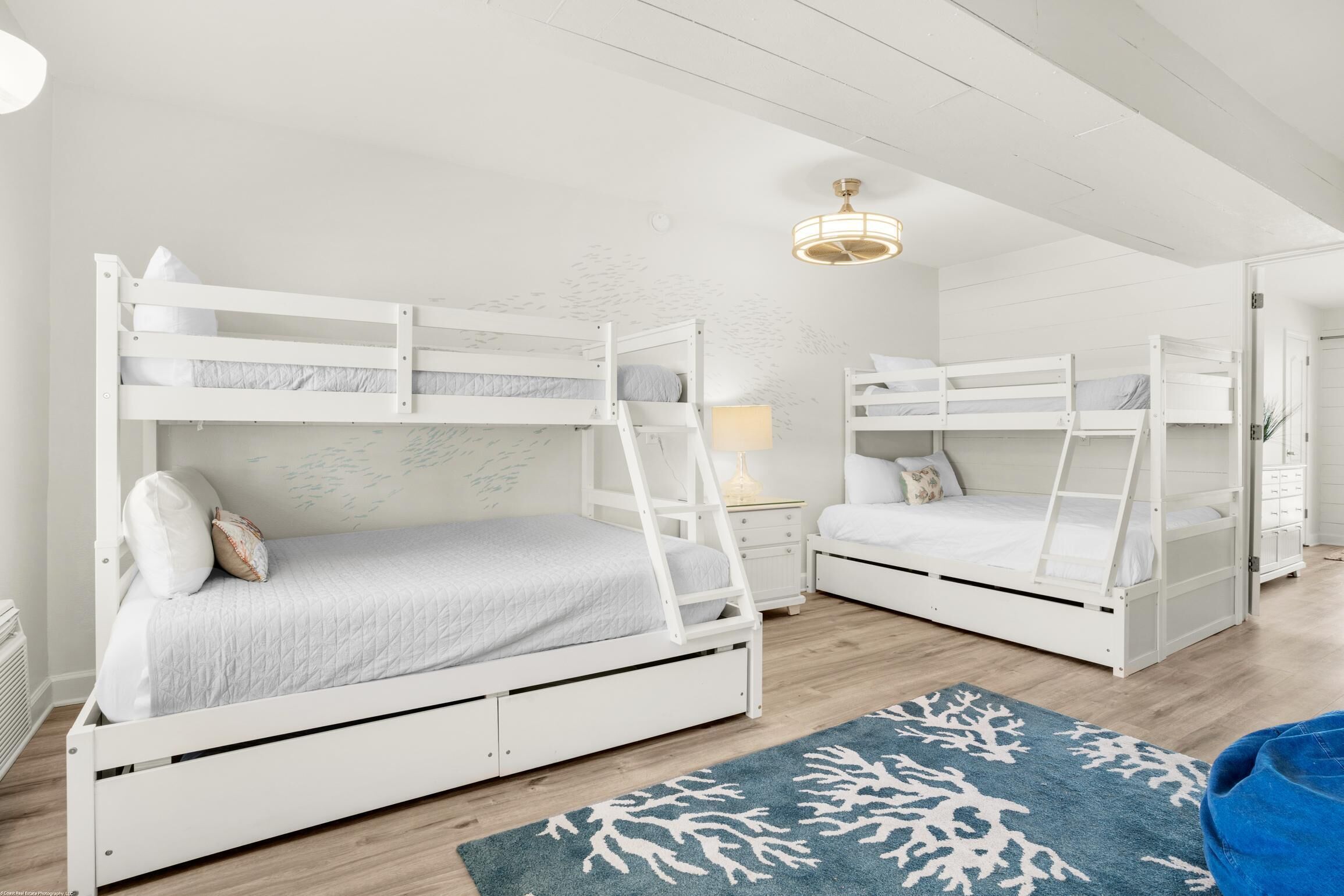 A room with two bunk beds, a nightstand with a lamp, and a blue patterned rug.