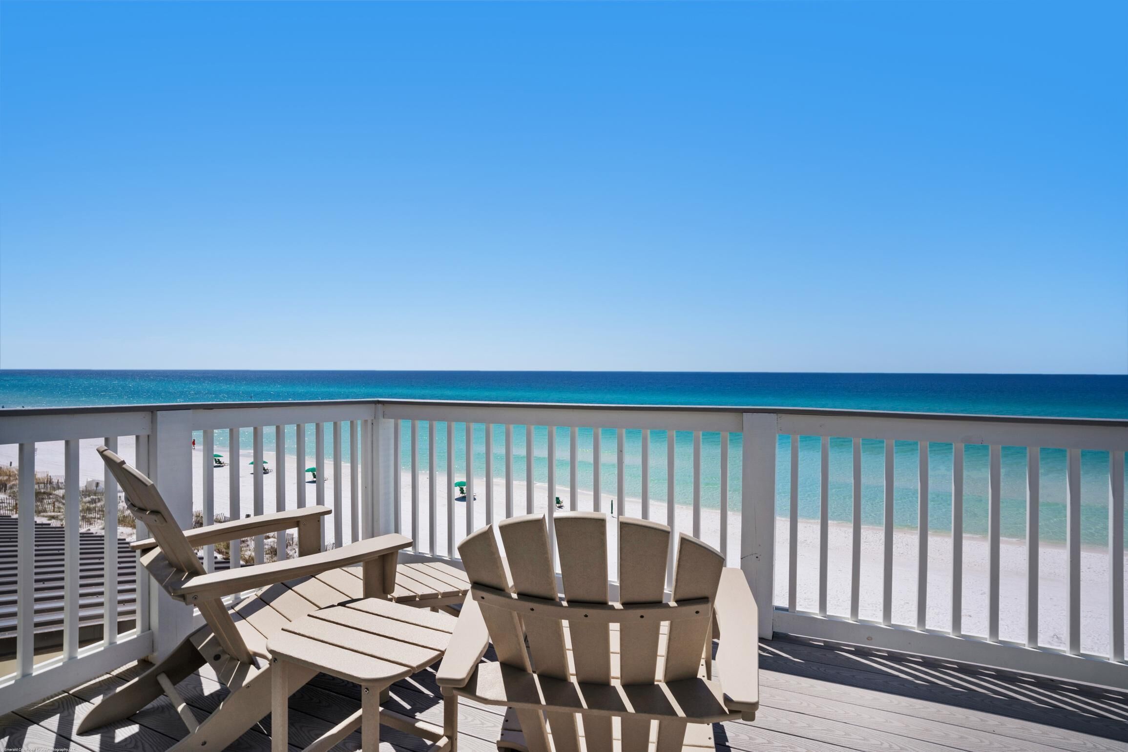 A wooden deck with two Adirondack chairs facing a beach.