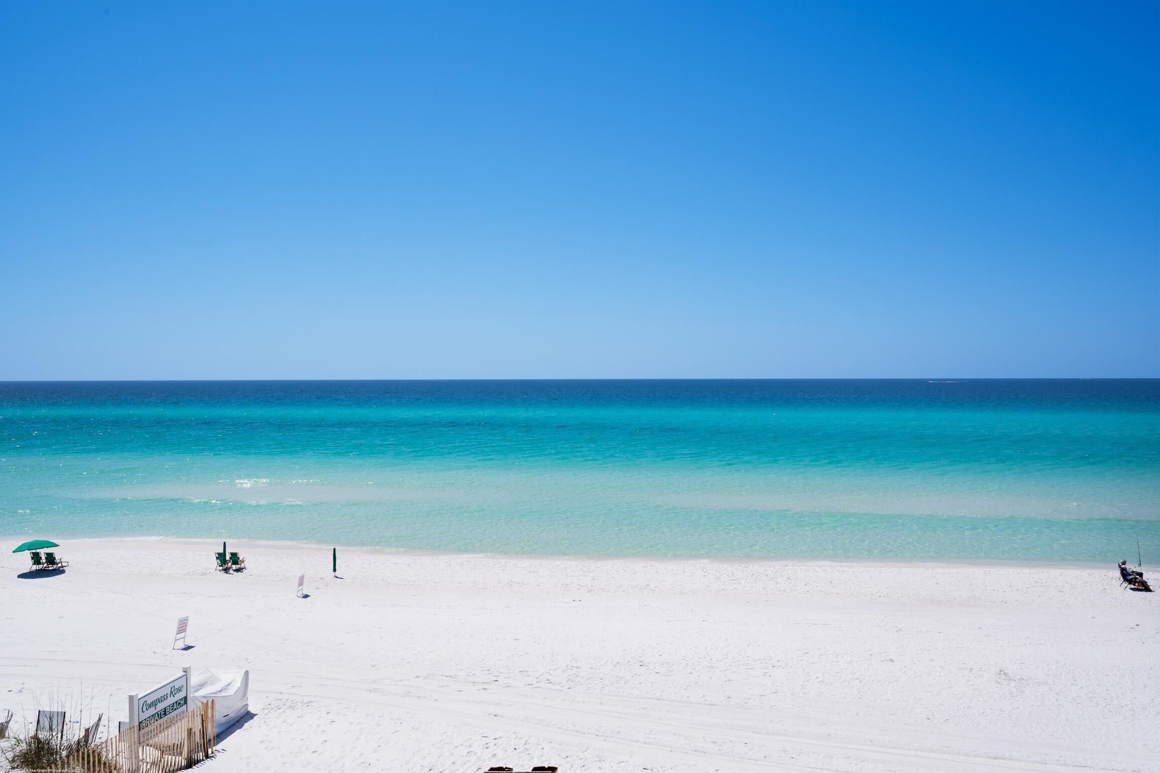 Une plage de sable blanc, avec une eau turquoise et limpide, quelques chaises de plage et des parasols.