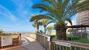 A wooden pathway leading to a beach area with palm trees and a sign indicating restrooms. - Hidden Dunes 1803 (Panama City Beach)