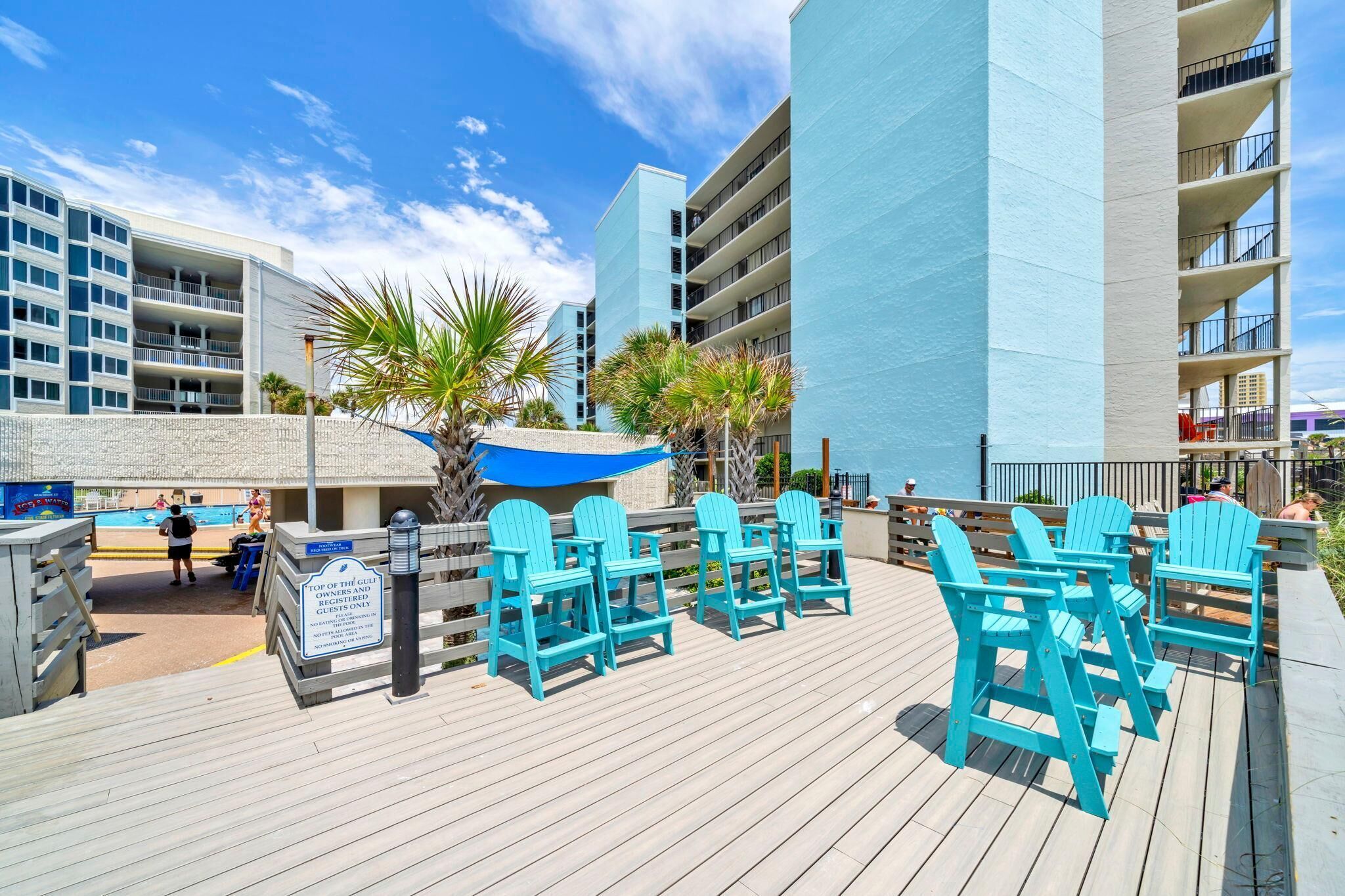 A poolside area with blue Adirondack chairs, a sign indicating it's a private area, and a building with multiple balconies in the background.