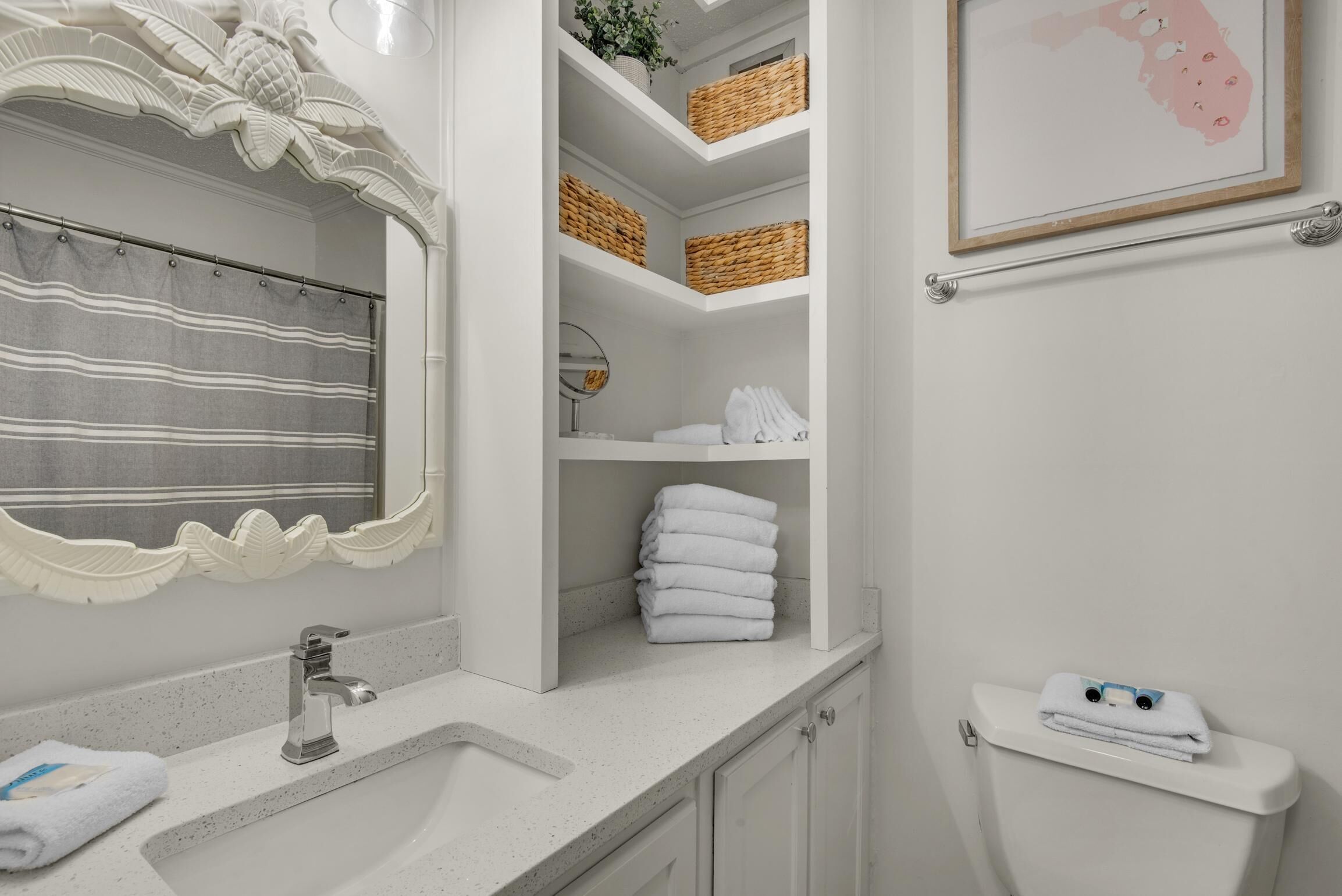 Une salle de bain avec un lavabo blanc, un miroir doté d’un cadre à motifs festonnés, un porte-serviettes et des toilettes sur lesquelles est posée une serviette.