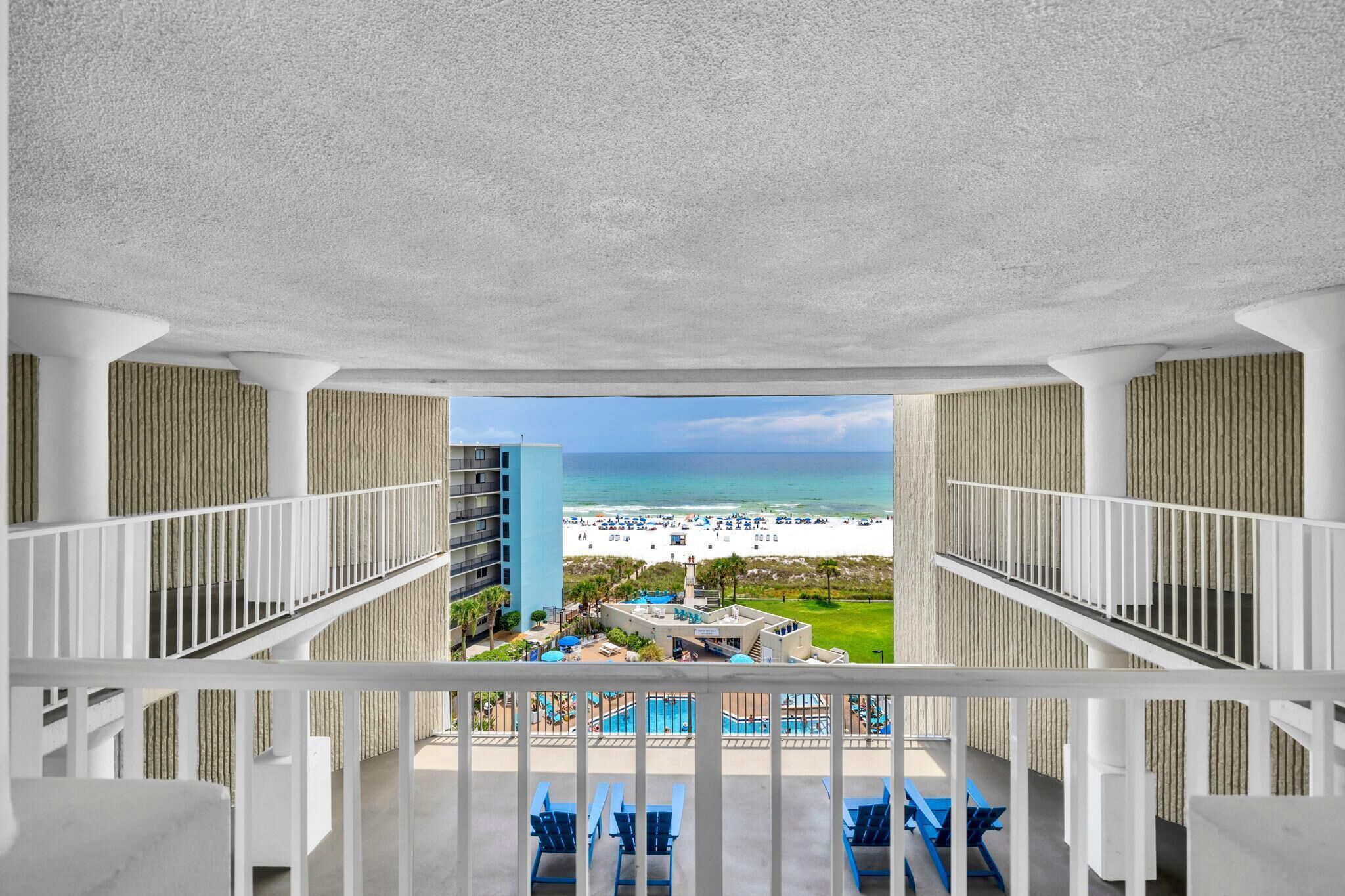 A hotel balcony with a view of a beach, pool, and adjacent buildings.