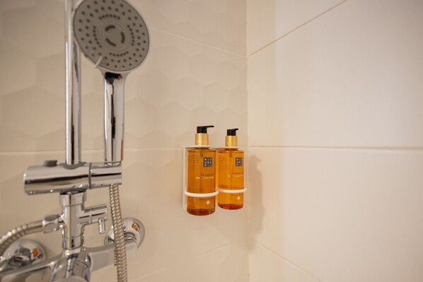 A bathroom with a shower, a handheld showerhead, and two bottles of shampoo and body wash mounted on the wall.