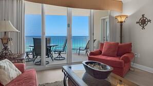 A room with a red sofa, a coffee table, and a view of the ocean through large sliding glass doors. - Emerald Beach 1036 - Turquoise Turtle (Panama City Beach)