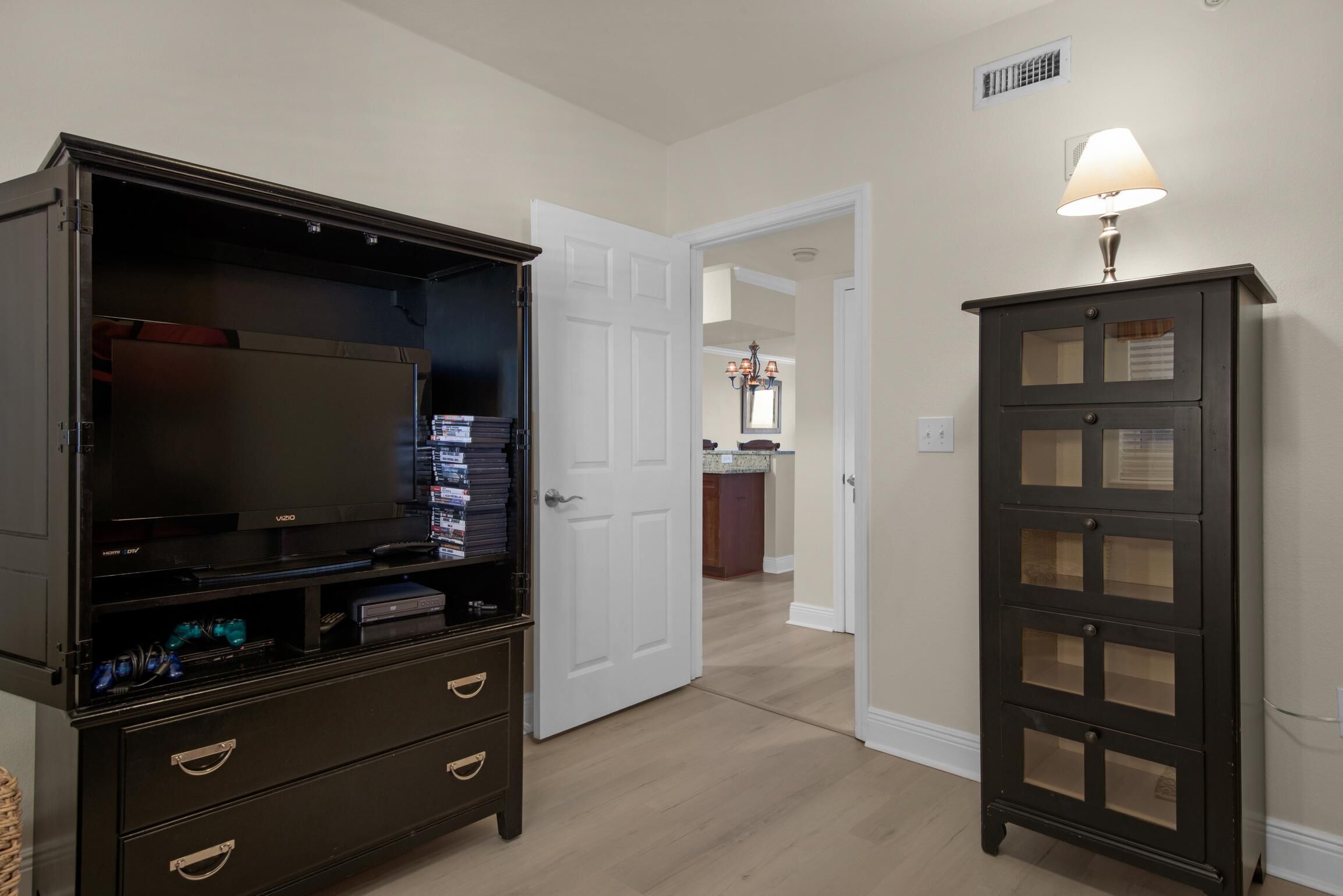 A room with a dark wooden entertainment center, a white door, and a small cabinet with a lamp.