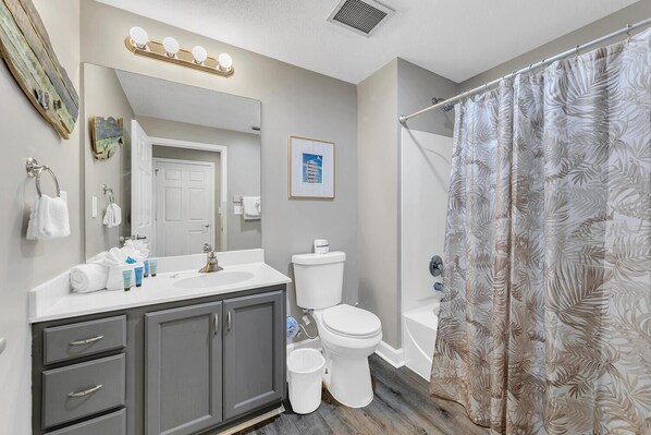 Une salle de bain comprenant un meuble-lavabo, un lavabo, un miroir, des toilettes et un rideau de douche.
