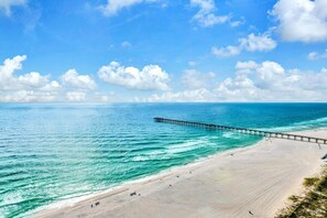 Een strand met een pier die zich uitstrekt over de oceaan, heldere lucht en kalm water.