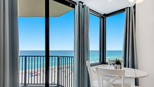Un balcone con vista sulla spiaggia, un tavolo con sedie e una ventola a soffitto.