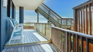 A wooden deck with a staircase leading to a higher level, a white railing, and a clear blue sky in the background. - Mainsail 101 (Miramar Beach)
