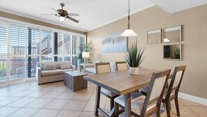 A spacious living area with a wooden dining table, beige sofas, and a ceiling fan. - Mainsail 101 (Miramar Beach)