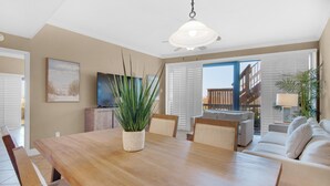 A dining area with a wooden table, chairs, a potted plant, and a television on the wall. - Mainsail 101 (Miramar Beach)