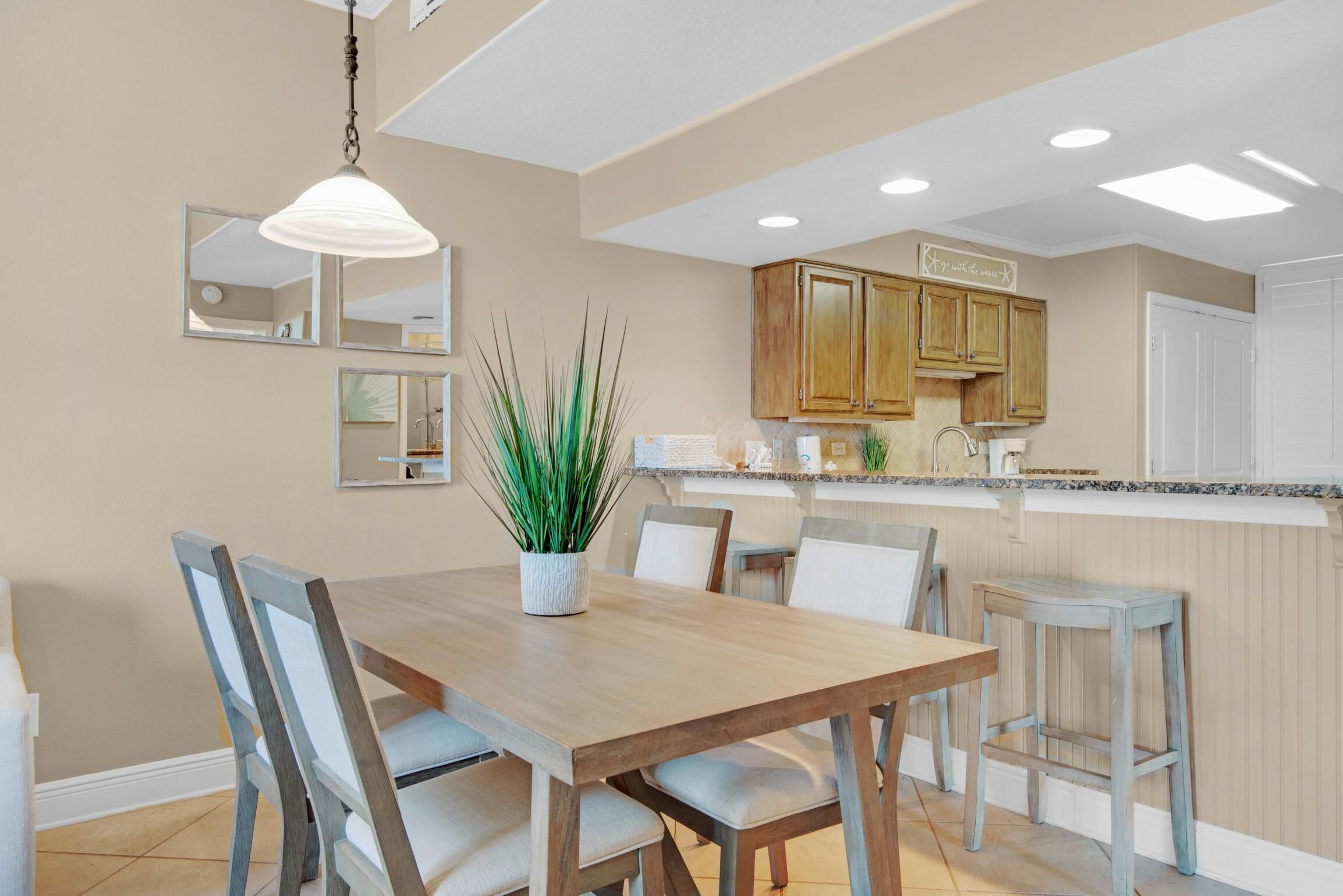 Un comedor con una mesa y sillas de madera, una planta en maceta y una cocina al fondo.