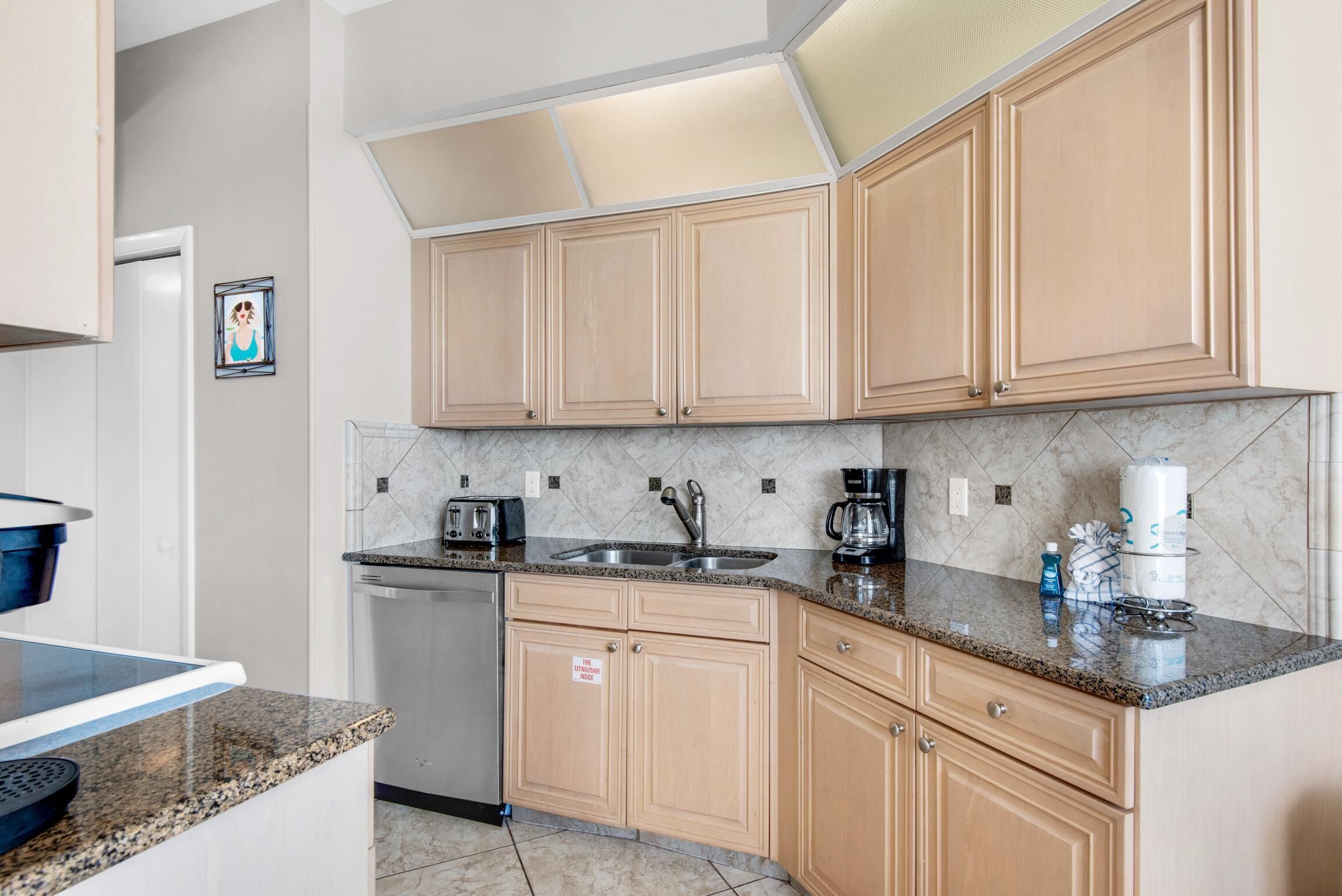 A kitchen with wooden cabinets, granite countertops, a coffee maker, and a dishwasher.