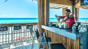 A beachside bar with a view of the ocean, metal chairs, and a bartender preparing drinks. - Surfside Resort #1509 (Miramar Beach)