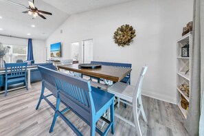 A modern dining area with a wooden table and blue chairs, a ceiling fan, and a decorative wall piece. - Rustic Oasis (Panama City Beach)