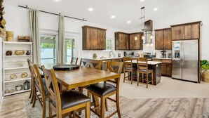 Una cocina moderna con armarios de madera, un refrigerador de acero inoxidable y una zona de comedor con mesa y sillas de madera.