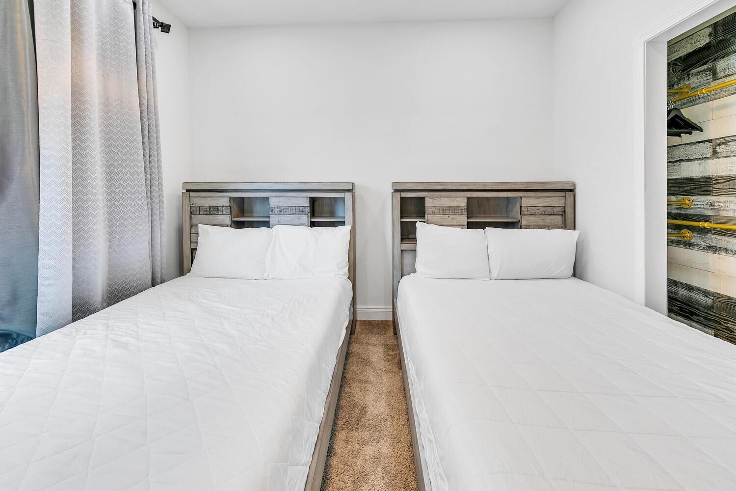 Quarto de hotel com duas camas de solteiro, cabeceira de madeira, carpete bege e uma grande janela com vista para um edifício.