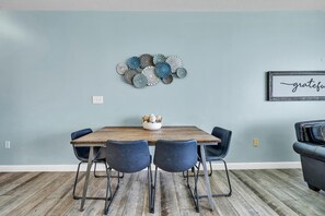 A dining area with a wooden table, four chairs, a decorative wall piece, and a framed sign. - Shores of Panama 1802 (Panama City Beach)