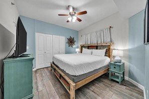 A bedroom with a wooden bed, a ceiling fan, a television on a stand, and a small bedside table with a lamp. - Shores of Panama 1802 (Panama City Beach)