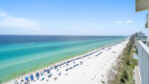 A beach with numerous umbrellas and sun loungers, a clear blue ocean, and a distant pier.