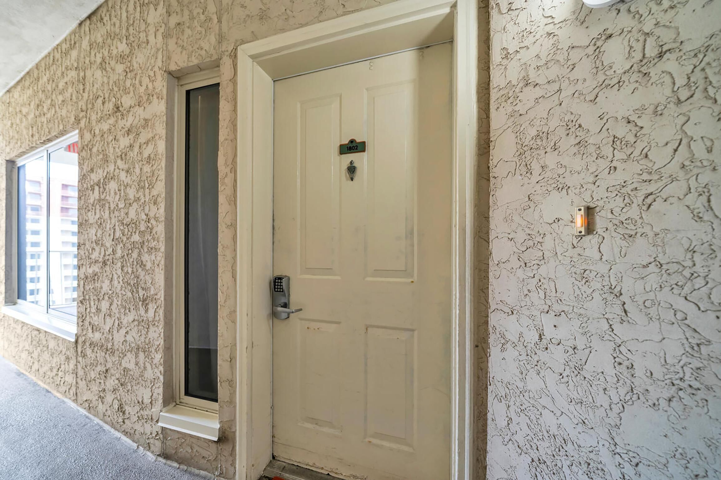 A white door with a keypad lock, a window to the left, and a textured wall.