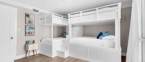 A bunk bed room with a white color scheme, a small bedside table, and a door.