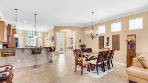 A spacious kitchen with a dining area, featuring a large island, bar stools, and a chandelier. - Wave N Sea (Destin)