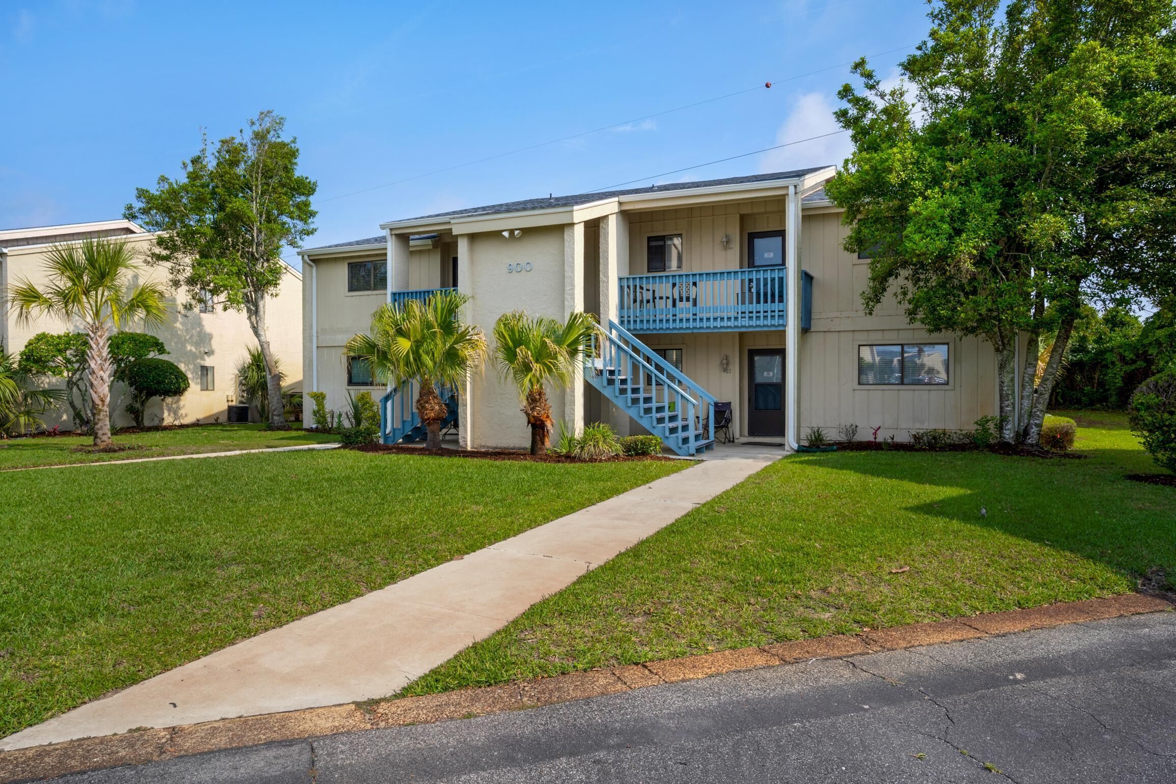 A two-story building with a blue staircase, numbered 900, and a small front yard with palm trees.
