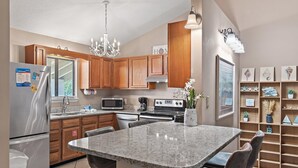 A modern kitchen with granite countertops, wooden cabinets, a stainless steel refrigerator, a microwave, a stove, and a dining area with a marble table and chairs. - Chateau La Mer II #904 (Destin)