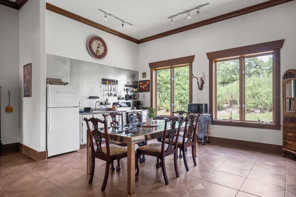 Une cuisine spacieuse dotée d’un îlot central, de chaises en bois, d’une horloge et de grandes fenêtres offrant une vue sur l’extérieur.
