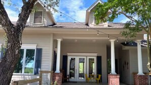 A two-story house with a covered front porch, a brick fireplace, and a small outdoor seating area with yellow chairs. - Cozy Guest House on Fitzhugh Rd in the Hill Country, 14 miles to downtown Austin (Austin)