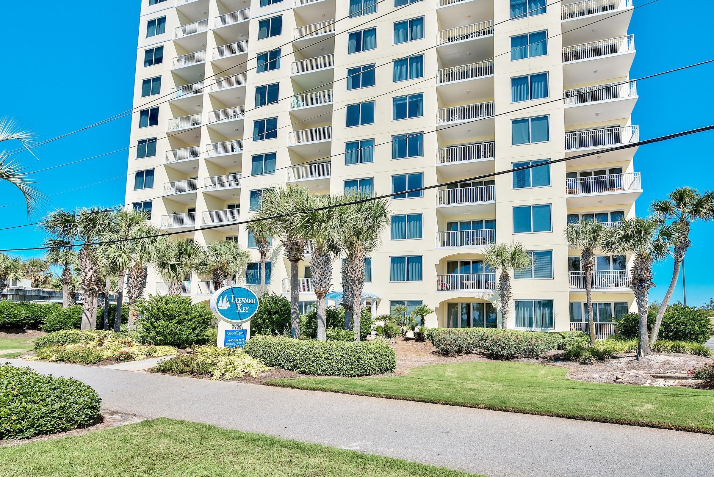 A multi-story hotel with balconies, surrounded by palm trees and well-maintained lawns.