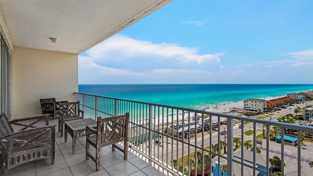 A balcony with wooden furniture overlooking a beach and ocean. - Leeward Key 1201 (Miramar Beach)