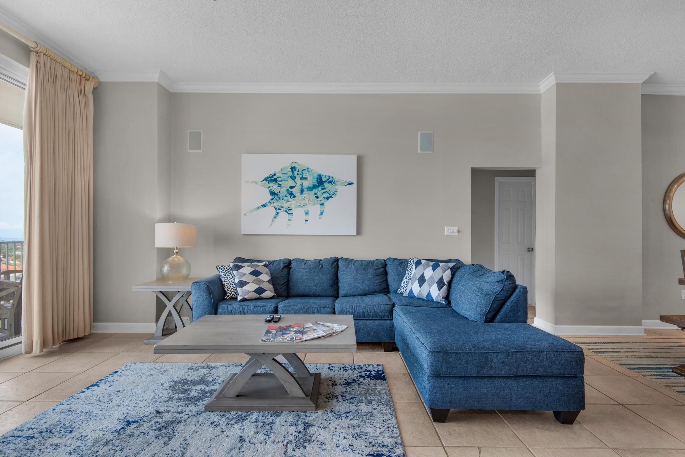 Uma sala de estar moderna com um sofá seccional azul, uma mesa de centro e uma janela grande com cortinas.