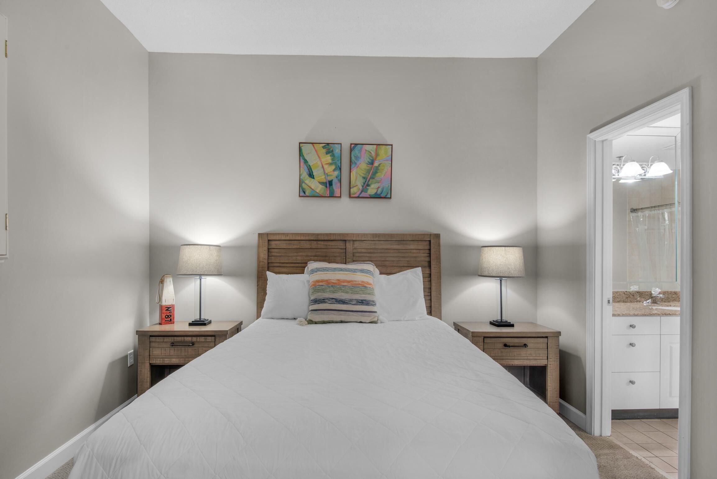 Une chambre à coucher avec un grand lit, deux tables de chevet avec des lampes, une tête de lit en bois et deux tableaux abstraits accrochés au mur.