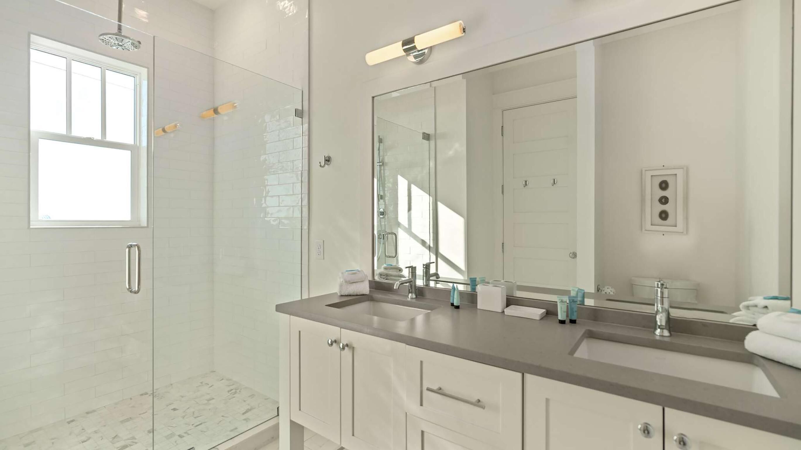 A modern bathroom with a glass shower enclosure, a large mirror, and a dual sink vanity.