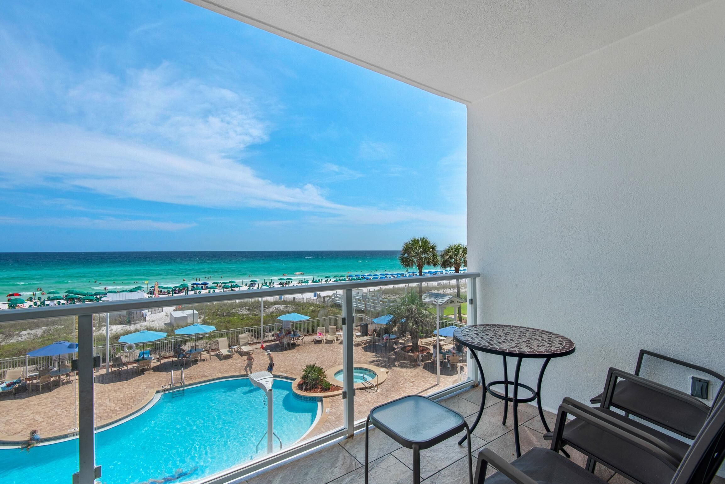 Un balcon avec vue sur une piscine et une plage, une table et des chaises.