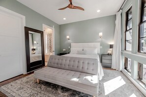 A bedroom with a bed, a bench, a ceiling fan, a mirror, and a window. - Paradise Pete's (Santa Rosa Beach)